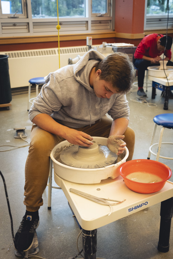 A pottery student throwing a pot on a wheel