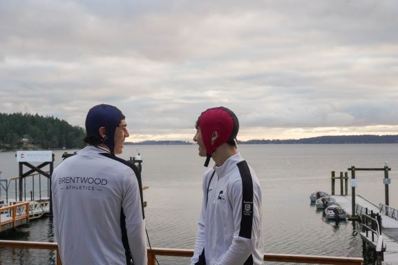 Two athletes in NeuroCatch caps laughing with docks and ocean behind