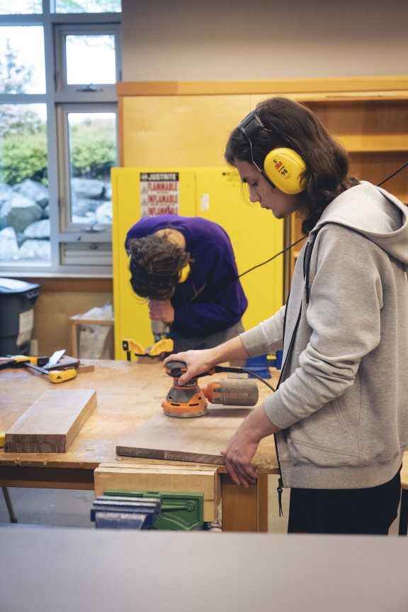 A student using a sanding tool on a plank of wood