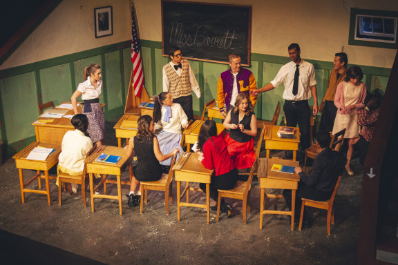 Students acting in a classroom set on stage