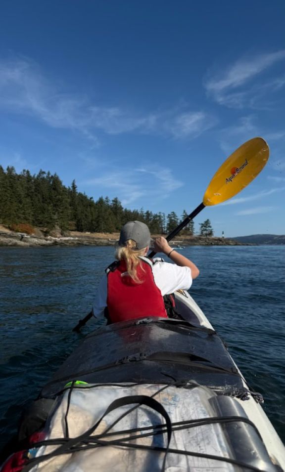We see from the kayakers point of view as we navigate towards a point over ocean water, a student with ponytail and paddle raisedcentre frame