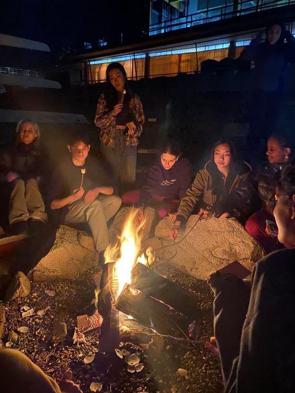Students enjoy roasting marshmallows over a beach fire on campus