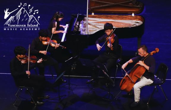 Students gathered around a grand piano, playing string instruments on stage