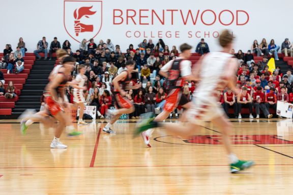 Sr Boys Basketball Team running down the court at a showcase game with crowd of fans behind