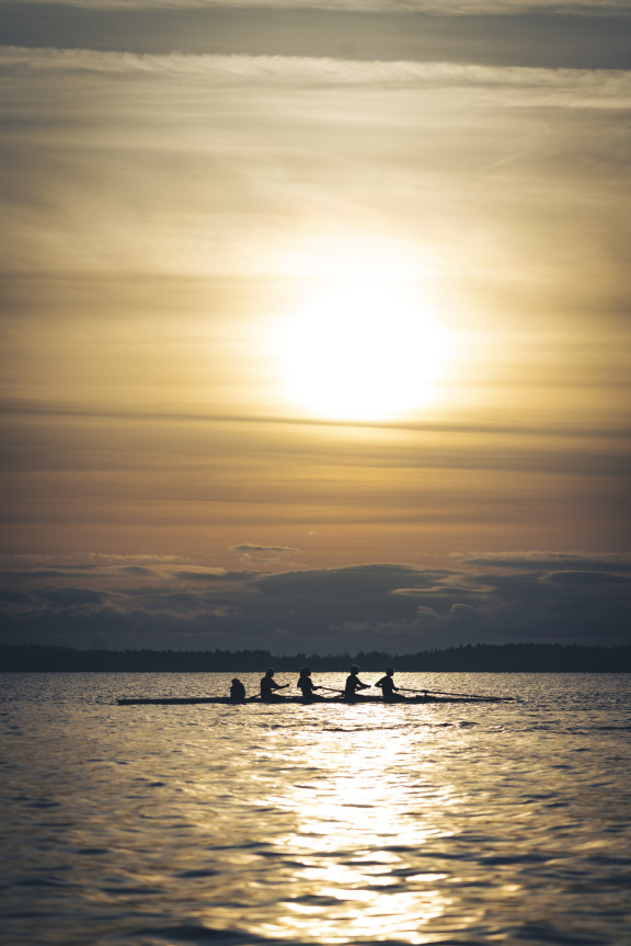 A boat of four rowers out on the water during a sunrise