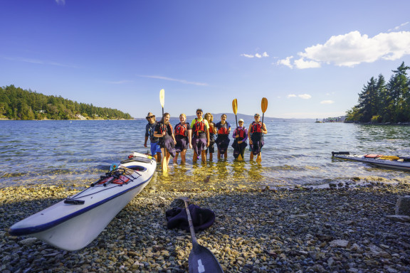 A group of kayaker standing on the beach while smiling
