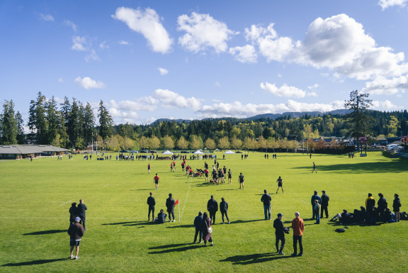 Coaches and players on Gillespie Field under a blue sky