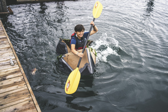 A student paddling a cardboard boat