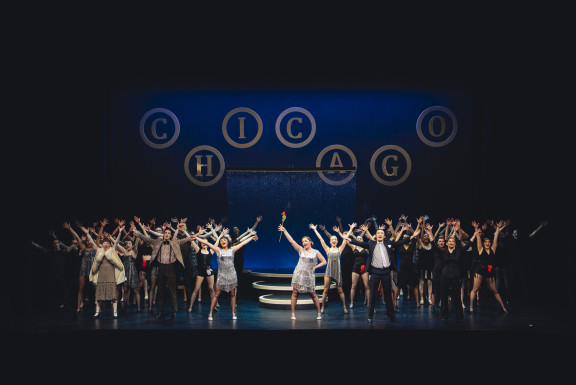 Students with their hands in the air during the musical production of Chicago