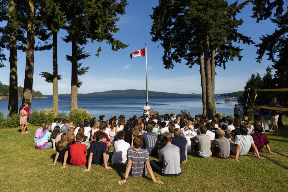Students sitting outside listening to the Head of School near the ocean