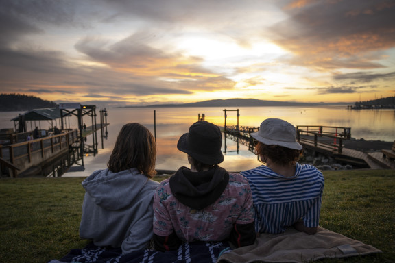 Three students sitting at the oceans edge looking at the sunrise