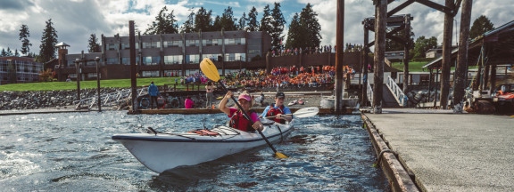 Students kayaking in front of a large crowd