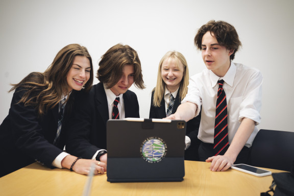 Four students smiling in front of a computer
