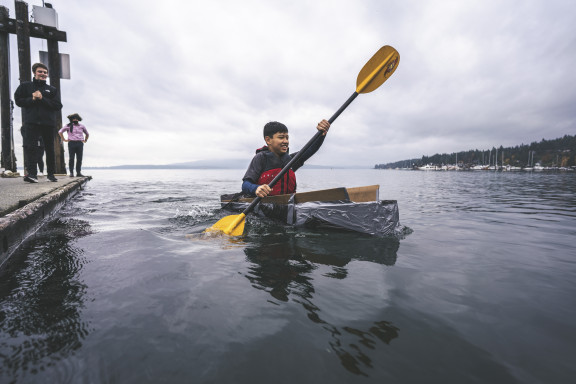 A student paddling a cardboard kayak