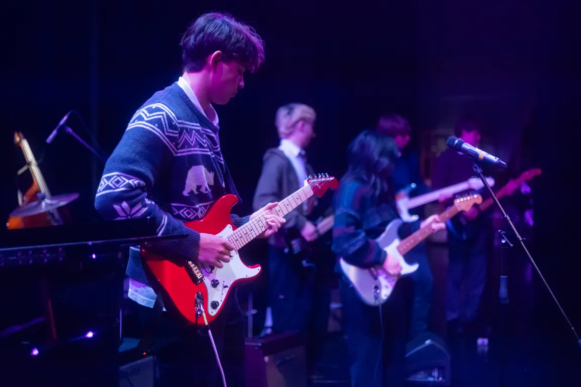 A student playing electric guitar in a band on stage