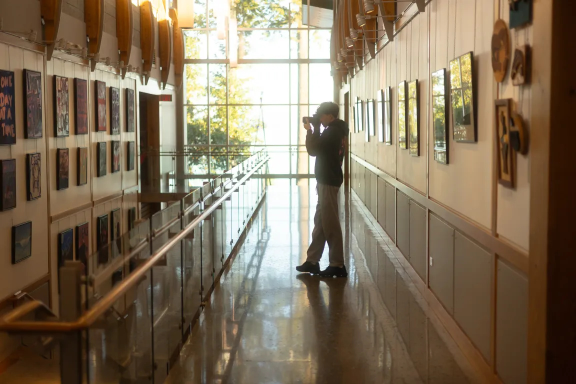 A photography student taking a photo in a sunlit art gallery hallway