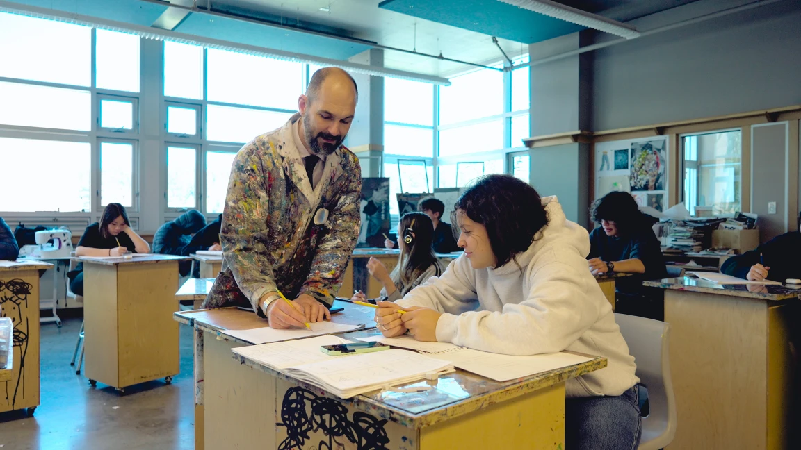 An art teacher helping a student at their desk in the drawing and painting studio