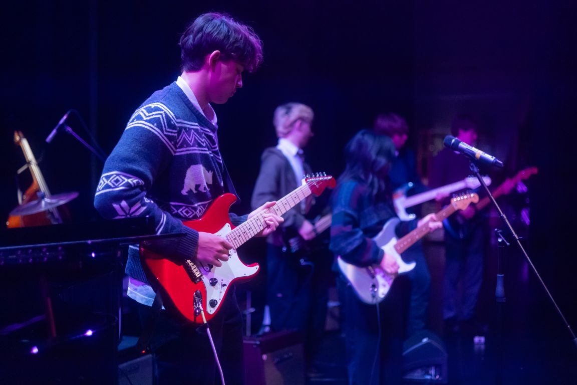 A student playing electric guitar in a band on stage