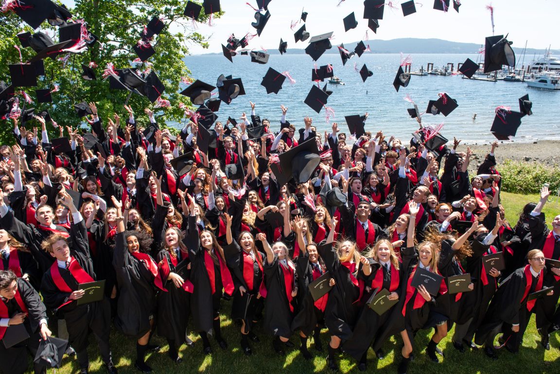 Graduating students tossing their caps in the air by the water