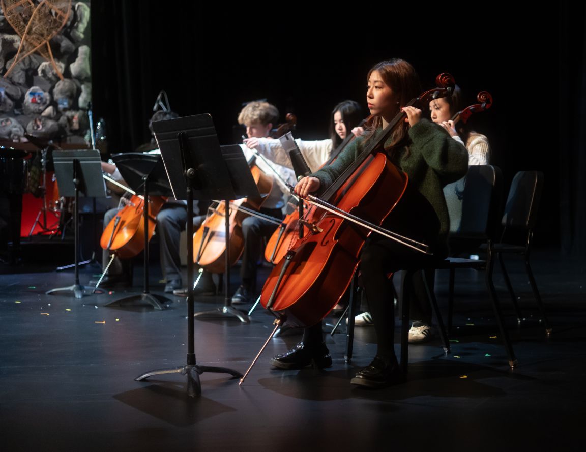 Boarding school students playing cellos in a string ensemble on stage