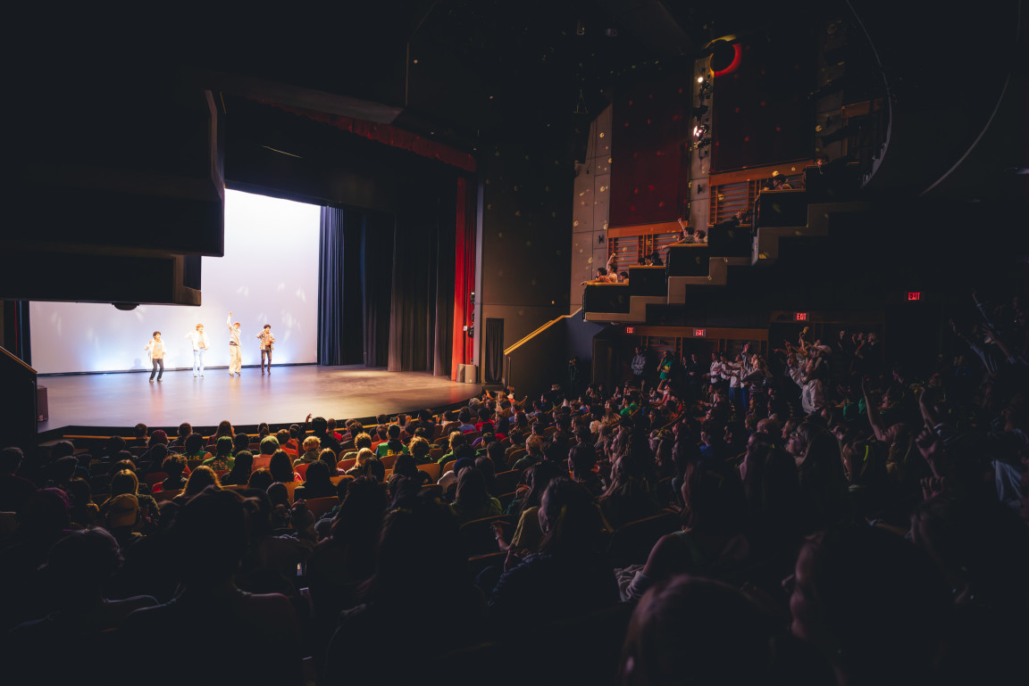 A packed theatre audience watching an Airband performance on stage