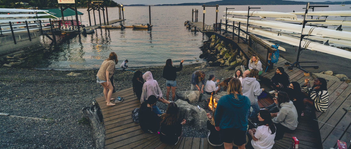 Students gathered around a fire on the dock at an Alex House bonfire