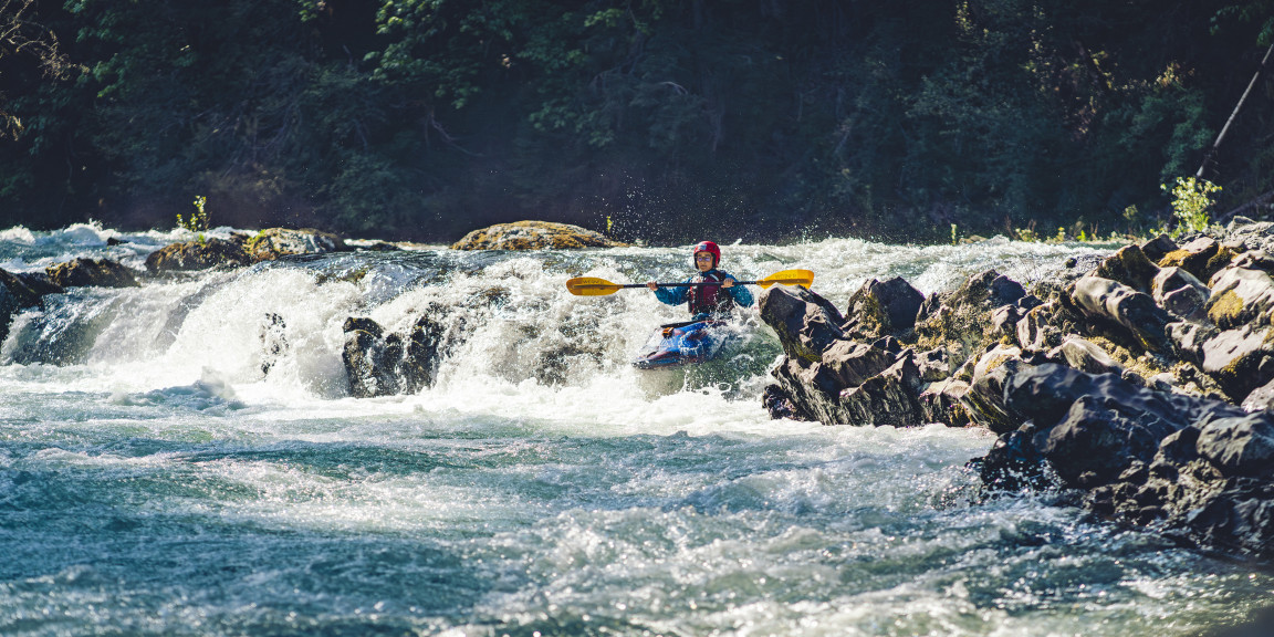 A student kayaking through whitewater rapids on the river