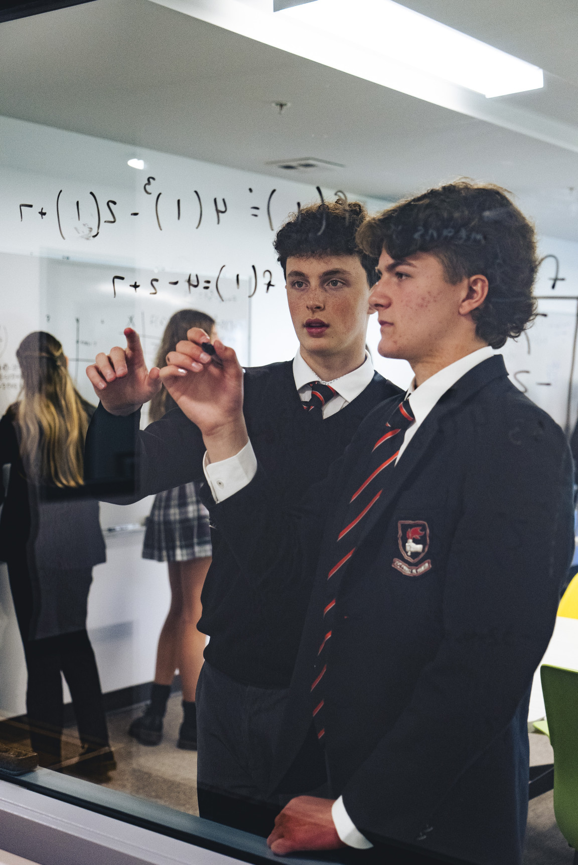 Two students working through a math problem on a glass writing wall