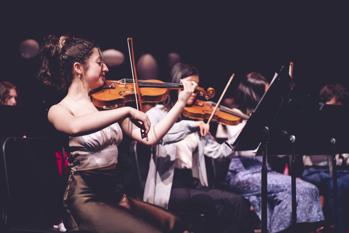 A student playing violin in an orchestra performance