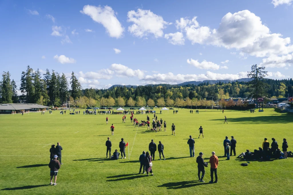 Coaches and players on Gillespie Field under a blue sky