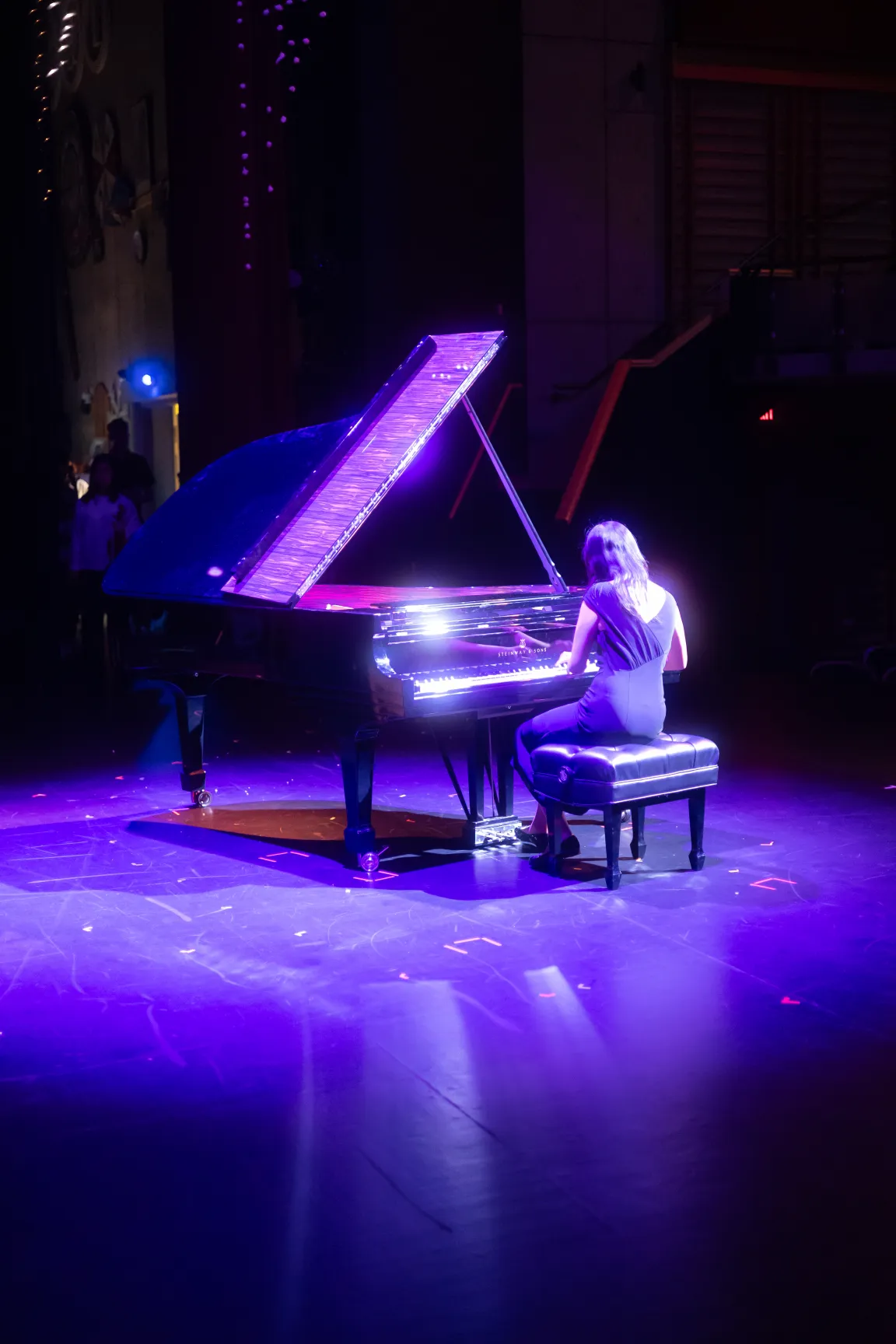 Boarding school student performing a grand piano solo on stage under coloured lights