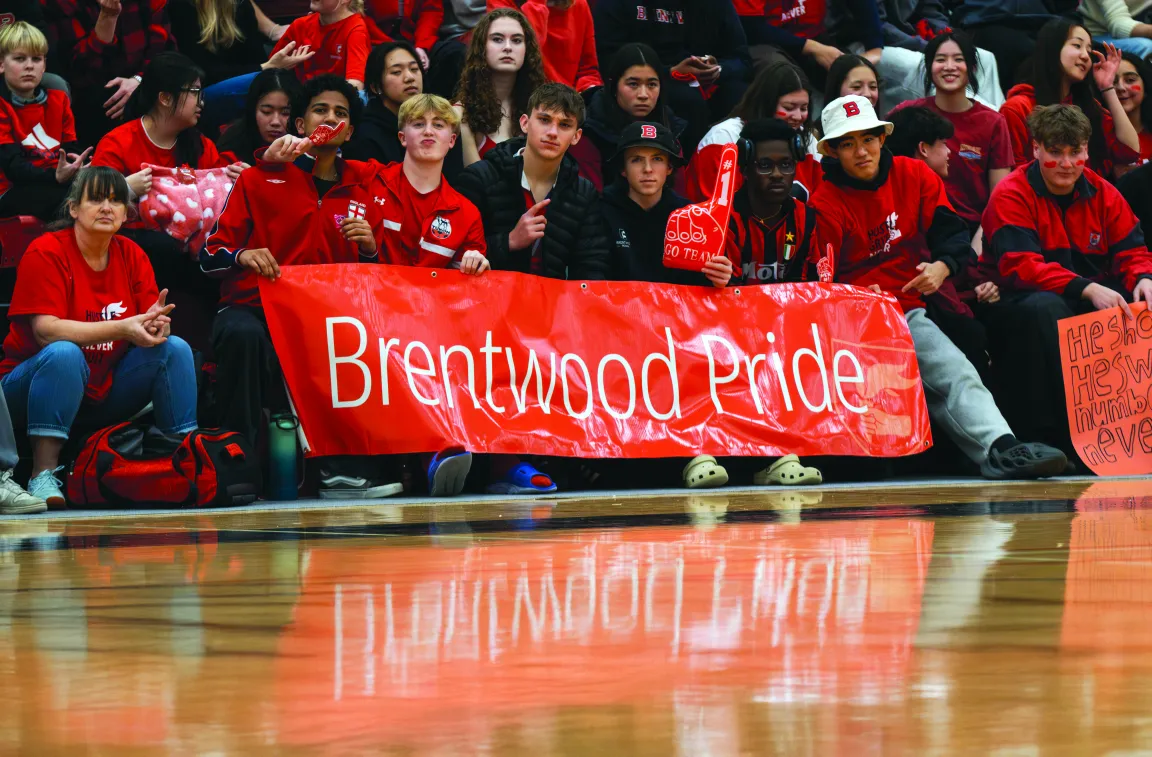 Students in red shirts sitting in bleachers holding a red banner that says Brentwood Pride