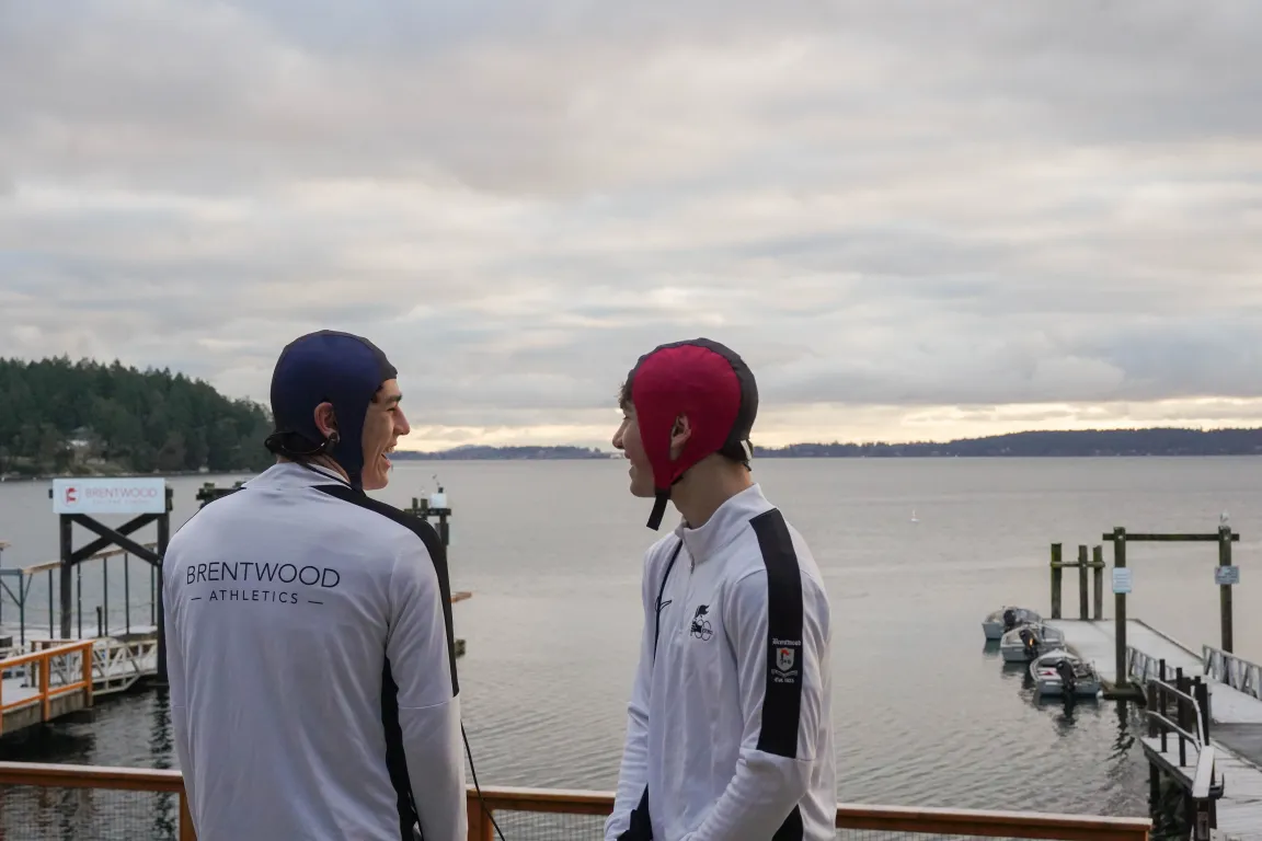 Two athletes in NeuroCatch caps laughing with docks and ocean behind