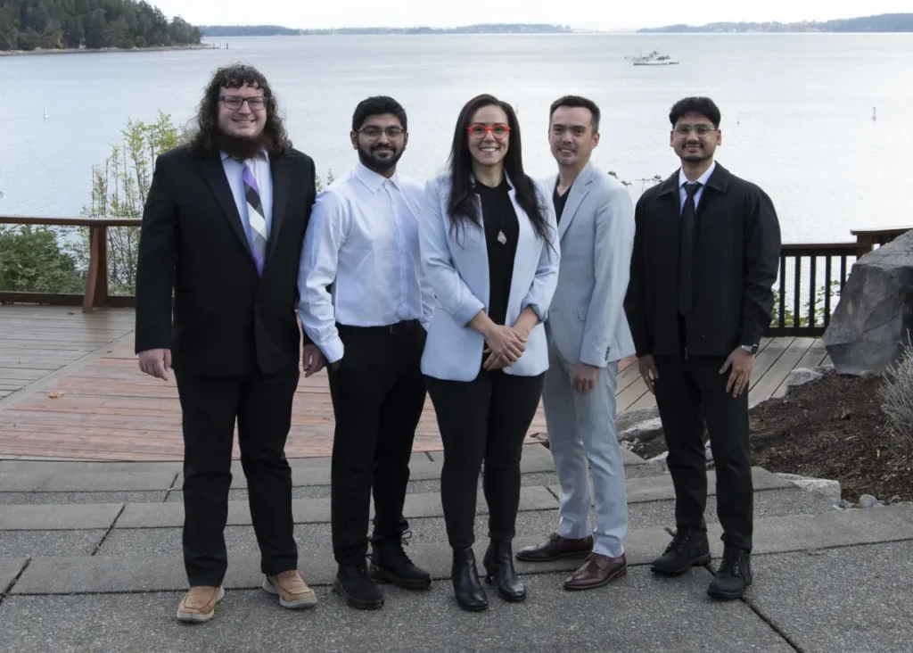 Five students in formal dress posing together by the water