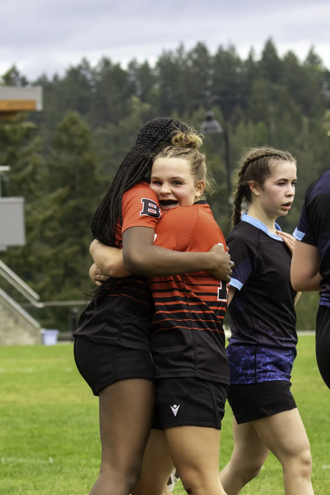 Two rugby players in orange and black jerseys embrace and smile on a field
