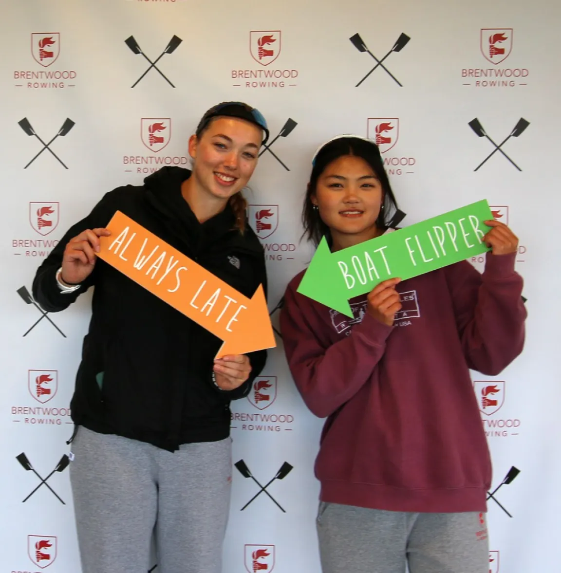 Two students posing at the Brentwood Rowing photo booth with fun signs