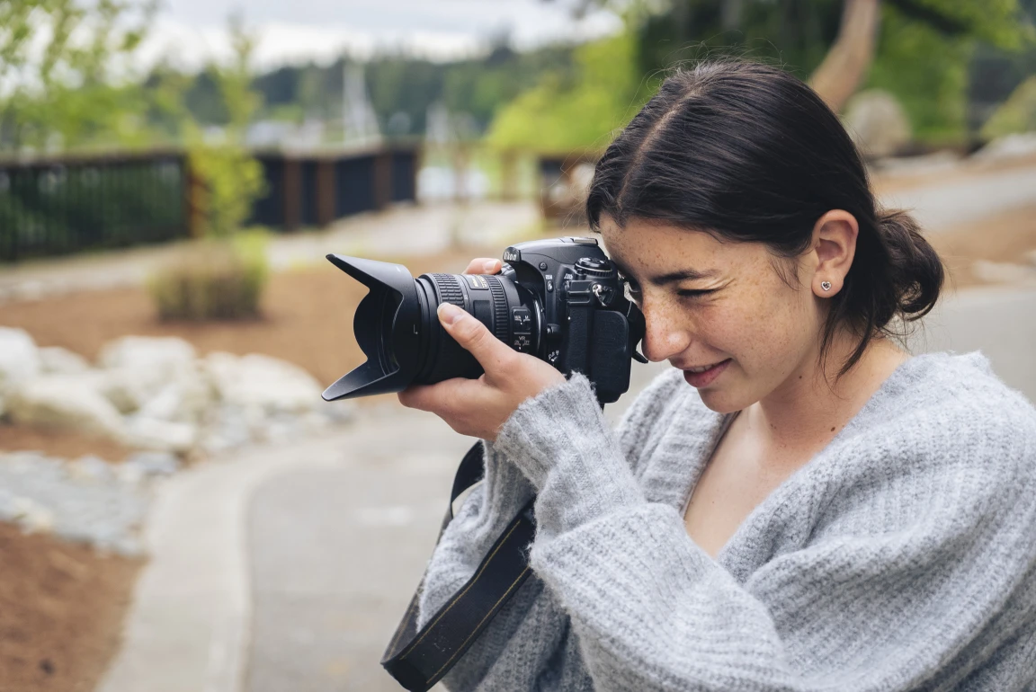 A photography student taking a picture outdoors with a camera