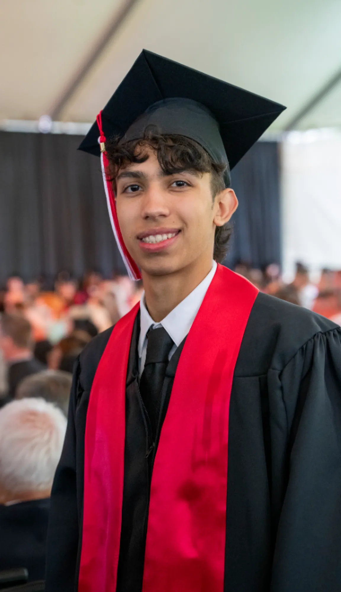 A graduating student in cap and gown with a red stole