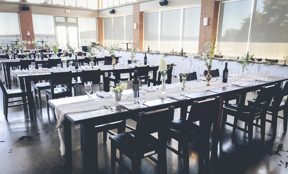 Brightly lit by the sun (floor to ceiling windows front and right), we can see tables set for dinner with a fully draped high table beyond