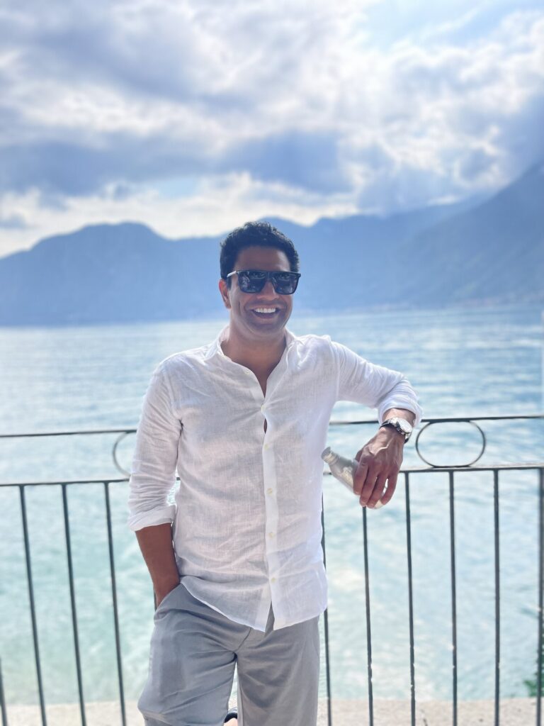 Rezwan Manji on a lakeside terrace with mountains behind him
