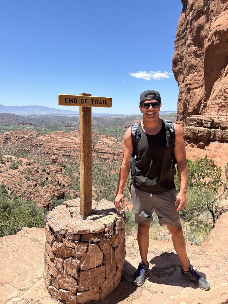 Rezwan Manji beside an End of Trail marker on a desert hike