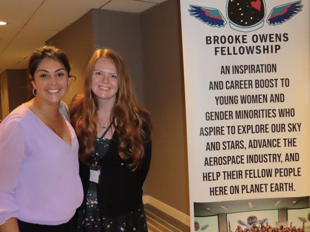Vanessa Van Decker with a colleague beside a Brooke Owens Fellowship banner